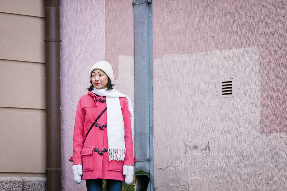 Hisayo Katsui, en japansk kvinna med ljusröd rock och vit scarf står framför en ljusröd byggnad.