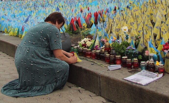 Kvinna böjer sig fram ett hav av ljus och blommor för krigets offer.