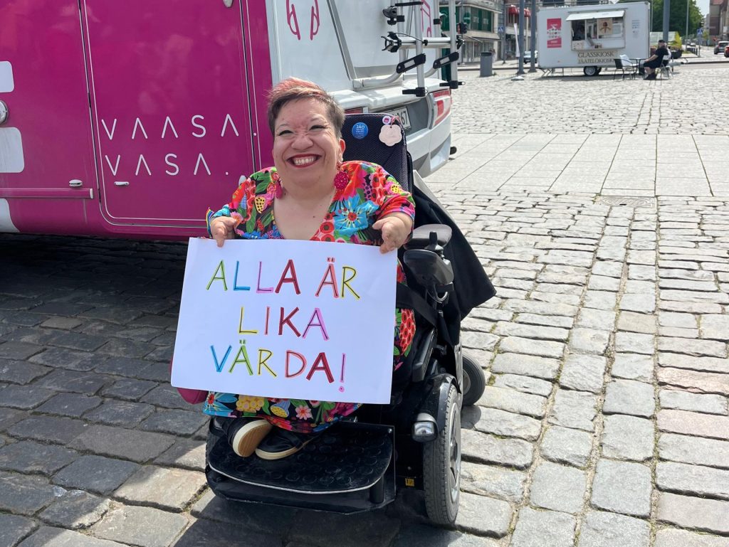 Koordinator Anna håller i ett plakat där det står: Alla är lika värda!
