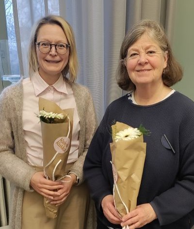 Ulrika Krook och Beatrice Wahlström står bredvid varandra och tittar in i kameran. Båda ler och håller en blomma i händerna. 